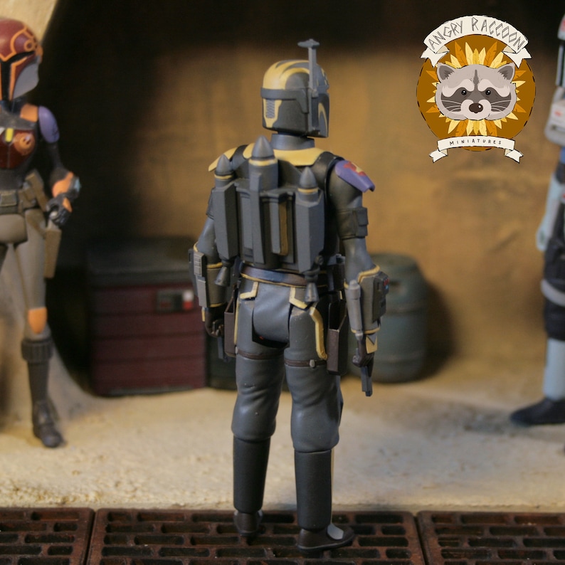 May include: A detailed action figure of a character in a dark gray and yellow armored suit, with a jetpack and sidearm holsters. The figure is posed in a gritty, industrial setting, with other figures in the background. The Angry Raccoon Miniatures logo is visible.