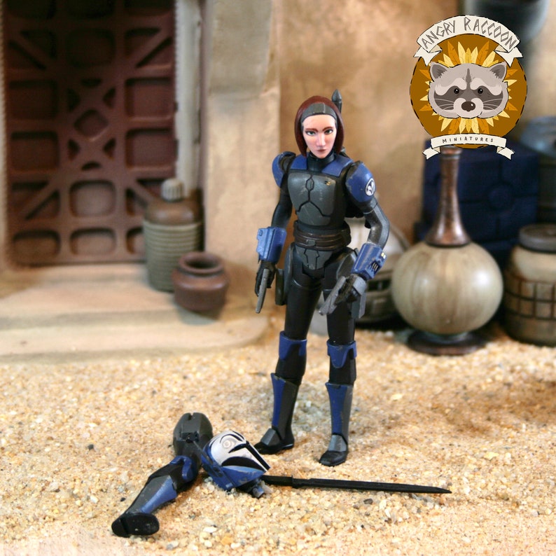 May include: A standing action figure with brown hair, wearing dark gray and blue armor with matching gauntlets. A detached blue and white helmet and a long black sword lie on the ground. A logo with a raccoon and the text ANGRY RACCOON MINIATURES.