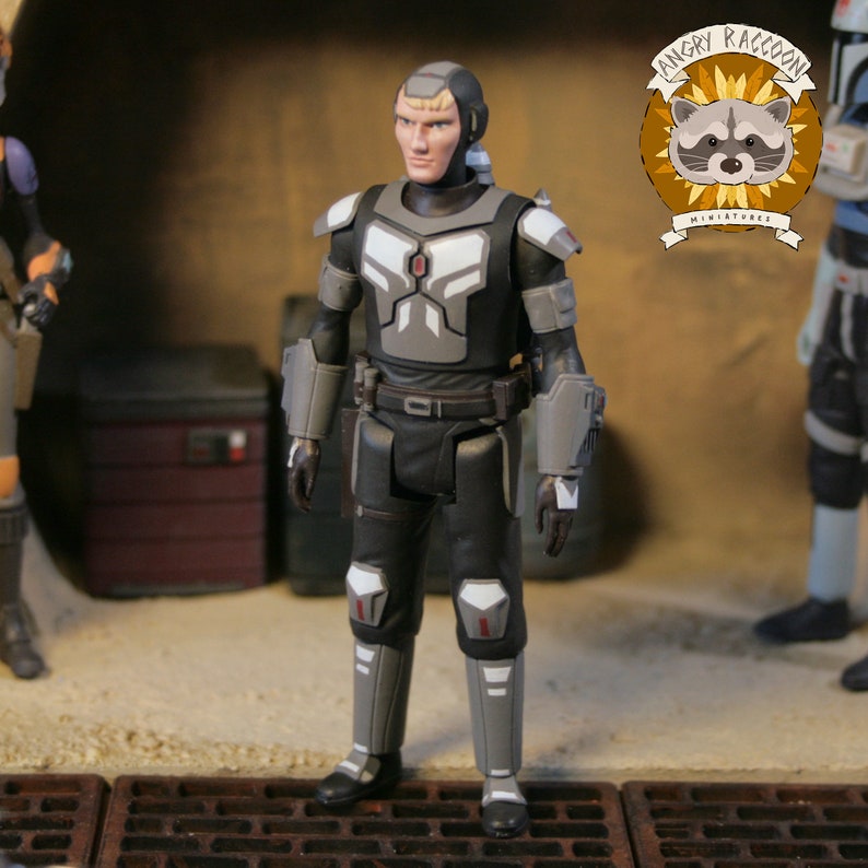 May include: A detailed action figure of a character in a black and gray armored suit. The figure has a blonde hairstyle and is standing in a diorama setting. The Angry Raccoon Miniatures logo is visible in the background.
