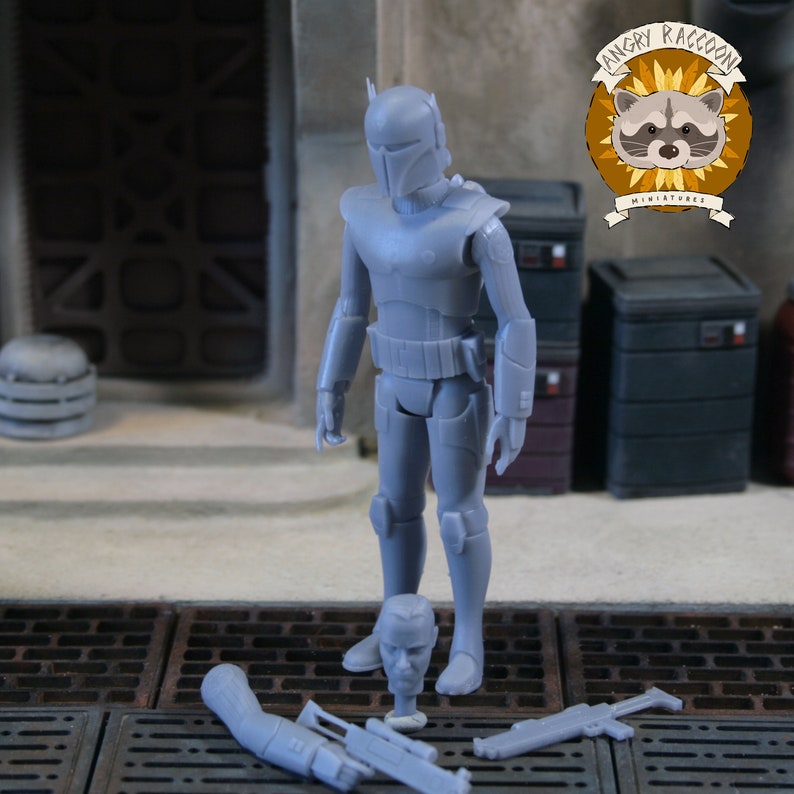 May include: A grey unpainted plastic action figure of a warrior in full armour with a T-shaped visor helmet. The figure stands upright with a separate unmasked head, a detached arm with a weapon, and a separate blaster rifle placed on the ground.