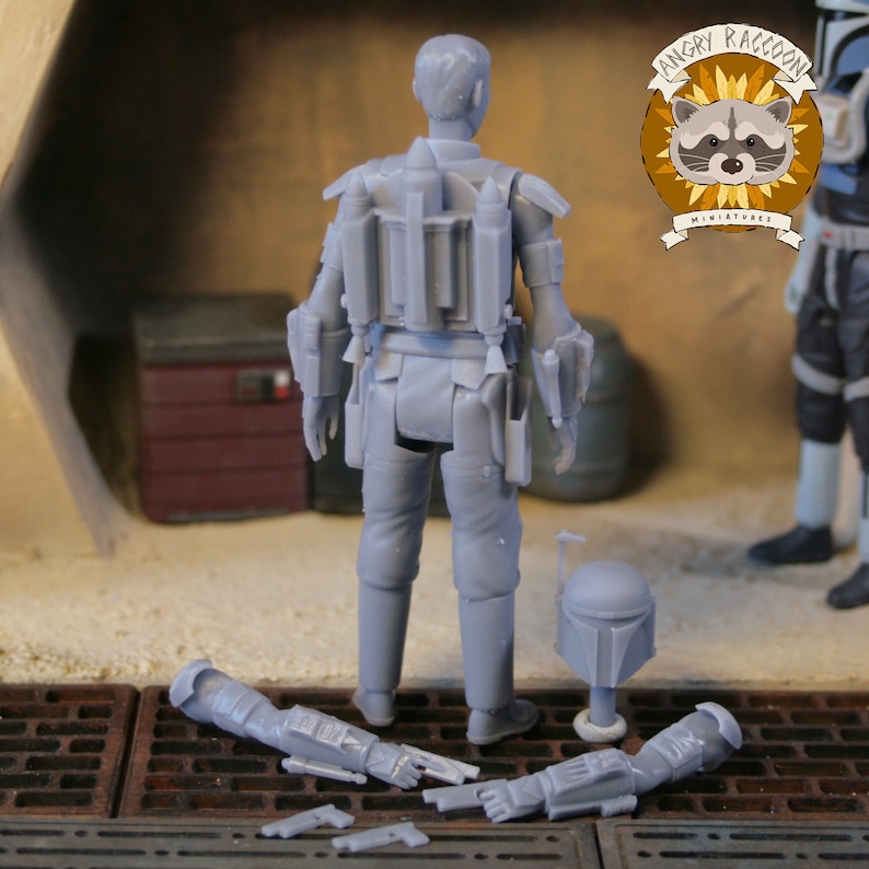 May include: A gray miniature figure of a character from a science fiction franchise, viewed from the back. The figure is wearing armor and has a helmet and detached arms. The Angry Raccoon Miniatures logo is visible in the background.
