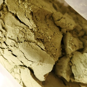 May include: Close-up of a bag of green powder. The powder is finely ground and has a slightly rough texture.