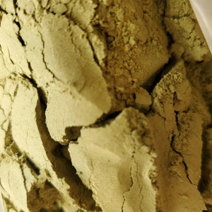 May include: Close-up of a bag of loose, light green powder. The powder is finely ground and has a slightly grainy texture.