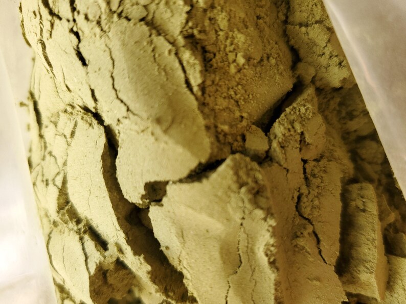 May include: Close-up of a bag of loose, light green powder. The powder is finely ground and has a slightly grainy texture.