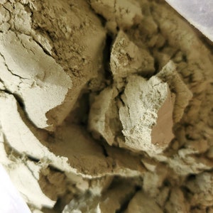 May include: Close-up of a pile of loose, light green powder. The powder is dry and crumbly, with a slightly rough texture.