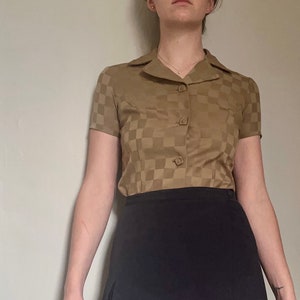 May include: A brown and tan checkered short-sleeved button-up shirt with a black mini skirt.