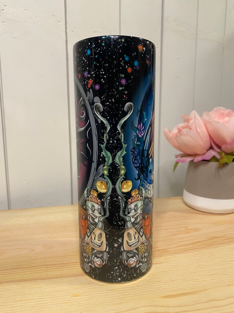 Peut inclure: Un gobelet cylindrique avec un fond bleu fonc&eacute; parsem&eacute; de points color&eacute;s. Le gobelet pr&eacute;sente un motif effrayant avec des personnages, des citrouilles et des &eacute;l&eacute;ments floraux. Les mots "There's" sont visibles sur le motif.