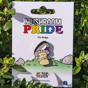 Peut inclure: Une carte blanche avec le texte "Mushroom Pride" en couleurs arc-en-ciel et un badge d'épingle en forme de champignon noir et blanc avec un design gris, blanc et violet. La carte comporte également le texte "Pin Badge" et "Hi Top Design" avec un champignon et le texte "#mushroompride".