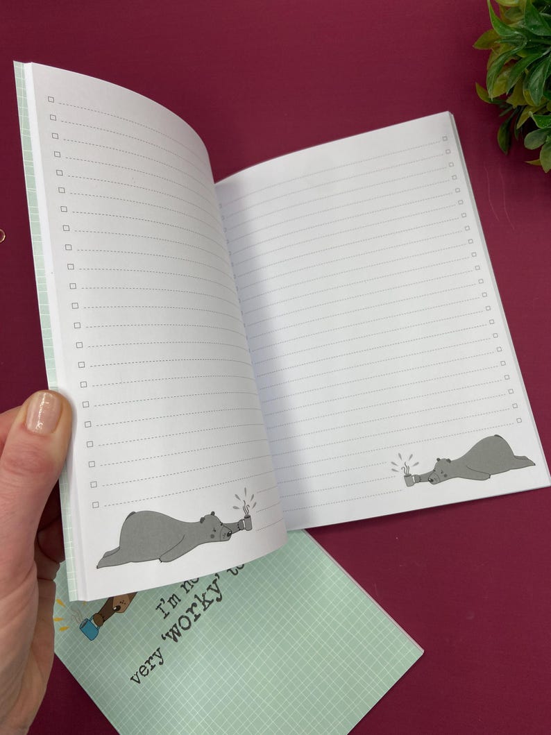 May include: Open notebook with lined pages and check boxes. The notebook features a light green cover with a grid pattern and the text "I'm not very 'worky'". Inside, a cartoon bear is drawn on the bottom of the pages, holding a mug.