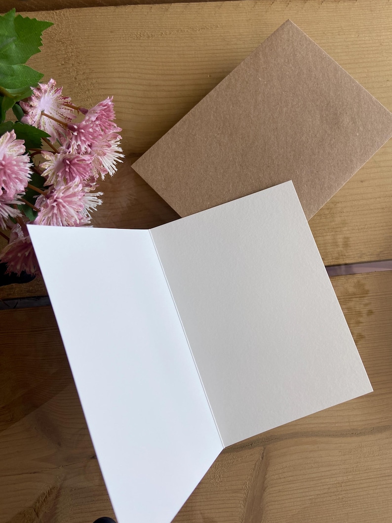 May include: A blank white card with a brown envelope. The card is folded in half and has a smooth, textured surface.