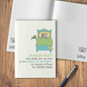 May include: A notebook featuring a cartoon cat in bed, with the text "random stuff that pops into my head in the middle of the night... my bedside offload for better sleep." A pen lies on a wooden surface.
