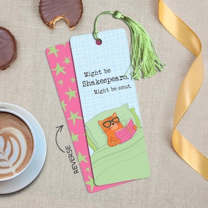 May include: A double-sided bookmark with a light green tassel. One side is light blue with a grid pattern, the text "Might be Shakespeare. Might be smut.", and an orange cat in glasses reading a pink book. The reverse is pink with green stars.