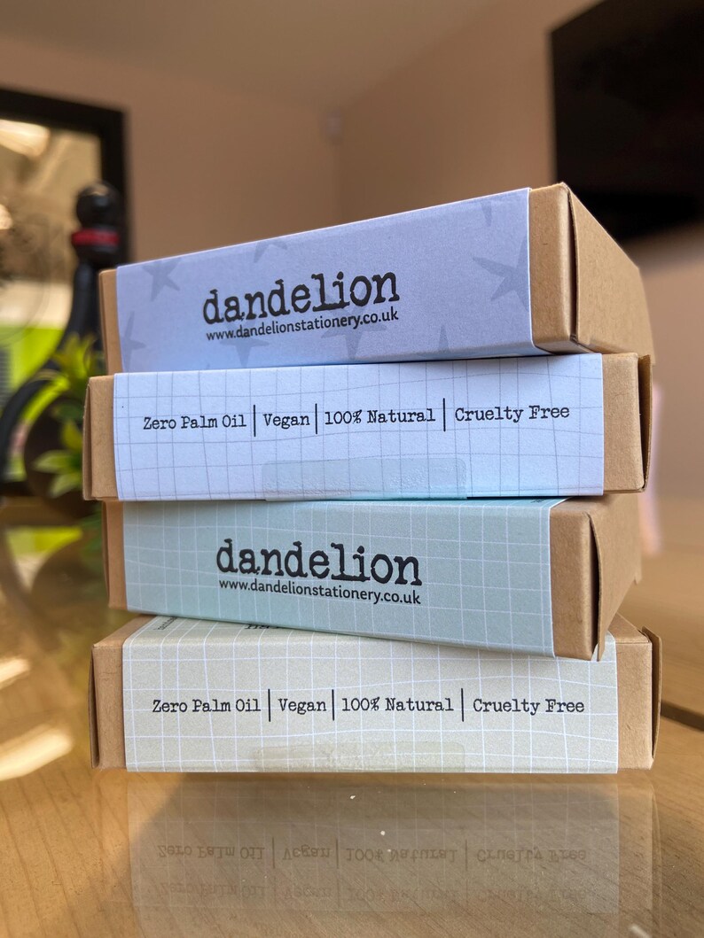 May include: Four stacked boxes of stationery products. The boxes are light brown with pastel-colored labels. The labels feature the brand name "dandelion" and the website address. The labels also state "Zero Palm Oil, Vegan, 100% Natural, Cruelty Free."