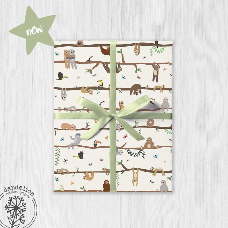 Puede incluir: Papel de regalo blanco con un patr&oacute;n repetido de perezosos colgados de ramas. Los perezosos est&aacute;n en varias poses, algunos est&aacute;n durmiendo, algunos est&aacute;n colgados boca abajo y algunos se est&aacute;n abrazando. Tambi&eacute;n hay tucanes y mariposas en el patr&oacute;n. El papel est&aacute; atado con una cinta verde.