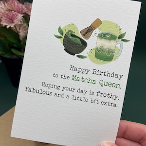May include: A white birthday card with the message "Happy Birthday to the Matcha Queen." The card includes illustrations of matcha tea, a whisk, and a mug. The card's message wishes a frothy and fabulous day.