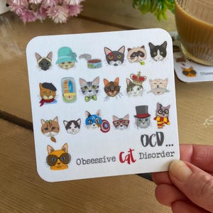 May include: White coaster with a colorful illustration of 18 cats with different accessories and expressions. The text "OCD... Obsessive Cat Disorder" is at the bottom of the coaster.