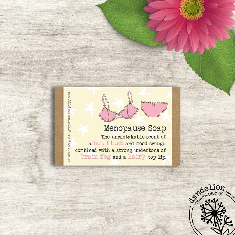 May include: A bar of handmade soap with a light yellow background and the words "Menopause Soap". The soap features a pink bra and underwear graphic. The text describes the scent as a "hot flush" and mood swings.