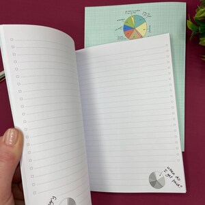 Puede incluir: Cuaderno abierto con p&aacute;ginas rayadas y casillas de verificaci&oacute;n. Presenta una cubierta verde claro e ilustraciones de gr&aacute;ficos circulares. El texto dice "Tengo hambre" y "&iquest;Cu&aacute;ndo me pagan?"