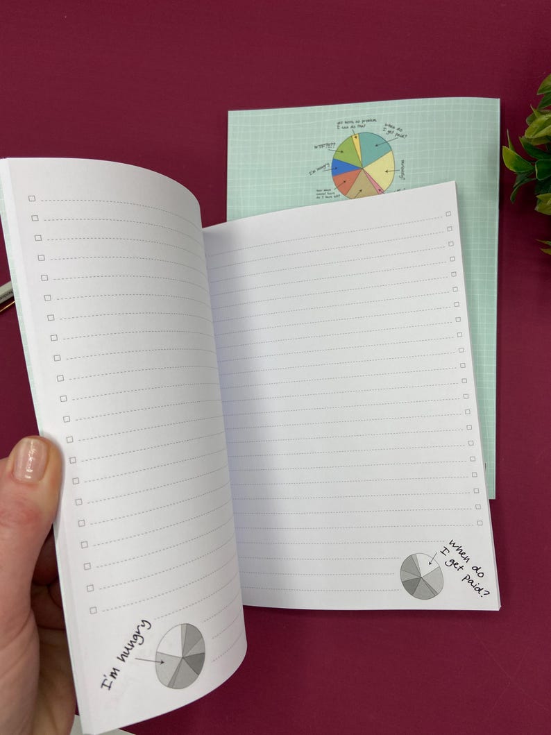 Puede incluir: Cuaderno abierto con p&aacute;ginas rayadas y casillas de verificaci&oacute;n. Presenta una cubierta verde claro e ilustraciones de gr&aacute;ficos circulares. El texto dice "Tengo hambre" y "&iquest;Cu&aacute;ndo me pagan?"