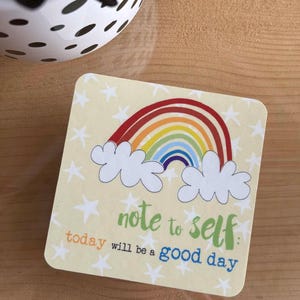 May include: A yellow square sticker with a rainbow, clouds, and stars. The text reads "note to self: today will be a good day."