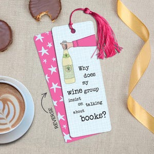 May include: A rectangular bookmark with a light blue grid pattern, a pink tassel, and an illustration of a hand holding a wine bottle. The text reads: Why does my wine group insist on talking about books? The reverse side is pink with white stars.