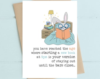 May include: A greeting card with a cartoon bunny in bed reading a book. The card says "You have reached the age where starting a new book at 9pm is your version of staying out until the bars close..."
