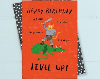 May include: A birthday card with a cartoon cat warrior riding a green dragon, set against an orange background. The card reads "Happy Birthday" and "Level Up!" with additional text indicating stat increases. The card is on a star-patterned background.