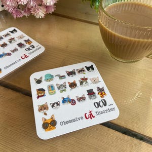 May include: White coaster with a design of 25 cartoon cats wearing different accessories and hats. The text "OCD... Obsessive Cat Disorder" is printed on the coaster.