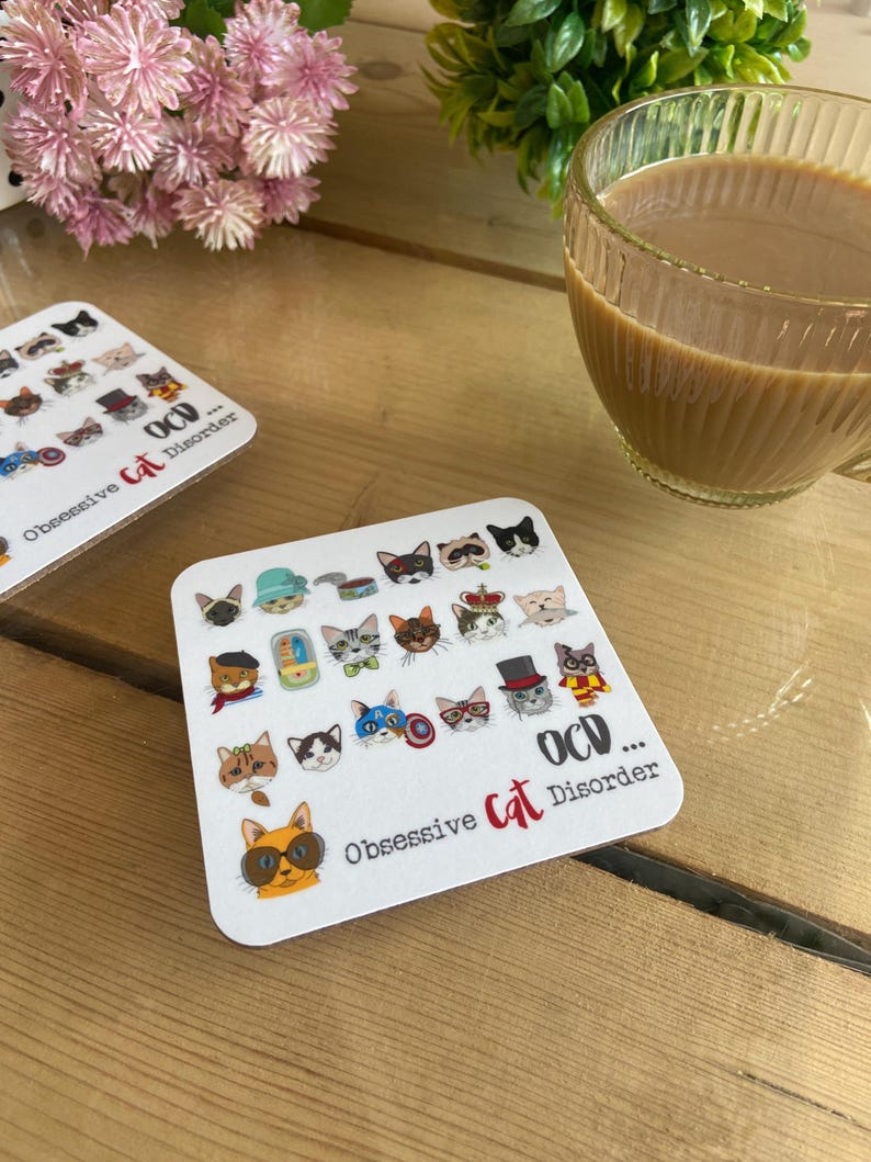 May include: White coaster with a design of 25 cartoon cats wearing different accessories and hats. The text "OCD... Obsessive Cat Disorder" is printed on the coaster.