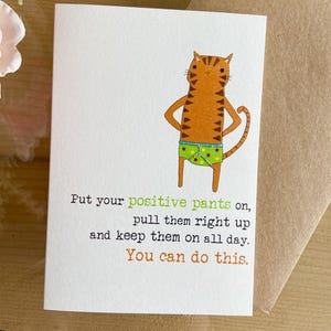 May include: A greeting card with a cartoon cat wearing underwear with stars on it. The card reads "Put your positive pants on, pull them right up and keep them on all day. You can do this."
