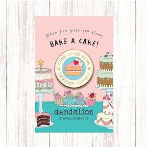 May include: A pink enamel pin badge with the text "When life gives you flour, BAKE A CAKE!" and "Cake Lover Club Lifetime Member". The pin features illustrations of cakes and cupcakes. The brand name "dandelion" is also displayed.