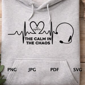 May include: A light gray hooded sweatshirt featuring a black graphic design of a heartbeat line, a heart shape with the text 911 dispatcher inside, and a headset icon. Below the heart, the text reads THE CALM IN THE CHAOS in black letters.