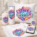 May include: A collection of white items with the text "Love Heals" in a colorful design. Includes a mug, tumbler, pillow, t-shirt, phone case, and a button. The design features hands, a heart, a cross, and leaves.