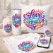 May include: A collection of white items with the phrase "Love Heals" in a colorful design. Items include a mug, tumbler, pillow, t-shirt, phone case, and a button. The design features hands, a cross, hearts, and leaves.