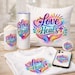 May include: A collection of white items with the text "Love Heals" in a colorful design. Includes a mug, tumbler, pillow, t-shirt, phone case, and a button. The design features hands, a heart, a cross, and leaves.