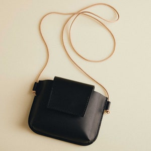 May include: A black leather crossbody bag with a long brown strap. The bag has a flap closure and a small pocket on the front.