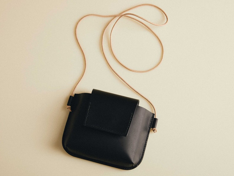 May include: A black leather crossbody bag with a long brown strap. The bag has a flap closure and a small pocket on the front.