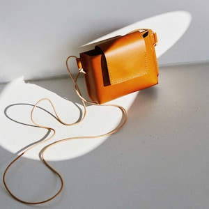 May include: A small, tan leather crossbody bag with a flap closure and a long strap.
