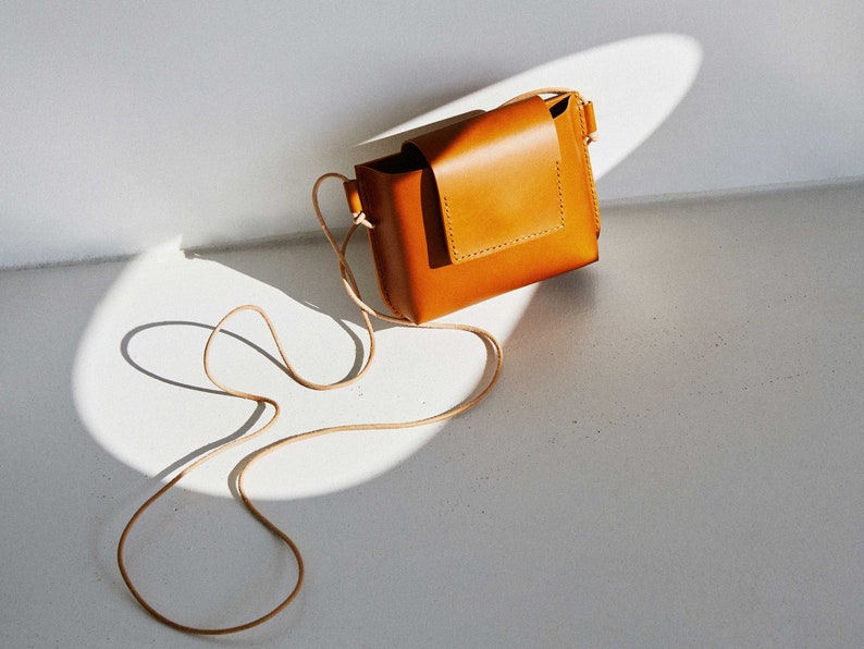 May include: A small, tan leather crossbody bag with a flap closure and a long strap.