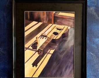 May include: A watercolor painting of a wooden acoustic guitar lying on a striped surface. The guitar is in the foreground and is the main focus of the painting. The background is a blurred image of a wooden surface. The painting is framed in a black frame.