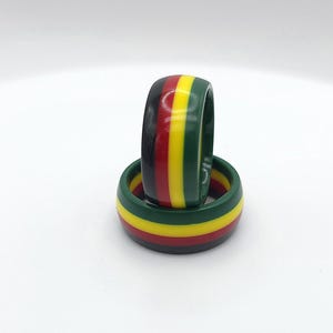 May include: Two stacked rings with a black, red, yellow, and green striped design.