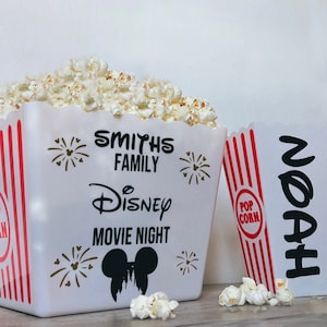Puede incluir: Dos contenedores de palomitas de maíz blancos con rayas rojas y blancas. Un contenedor tiene el texto "Smiths Family Disney Movie Night" con una cabeza de Mickey Mouse y fuegos artificiales. El otro contenedor tiene el texto "Noah" en negro.
