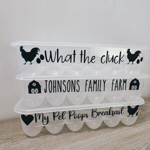 May include: Three clear plastic egg containers stacked on top of each other. Each container has a lid and is decorated with black graphics and text. The top container reads "What the cluck". The middle container reads "JOHNSONS FAMILY FARM". The bottom container reads "My Pet Poops Breakfast".