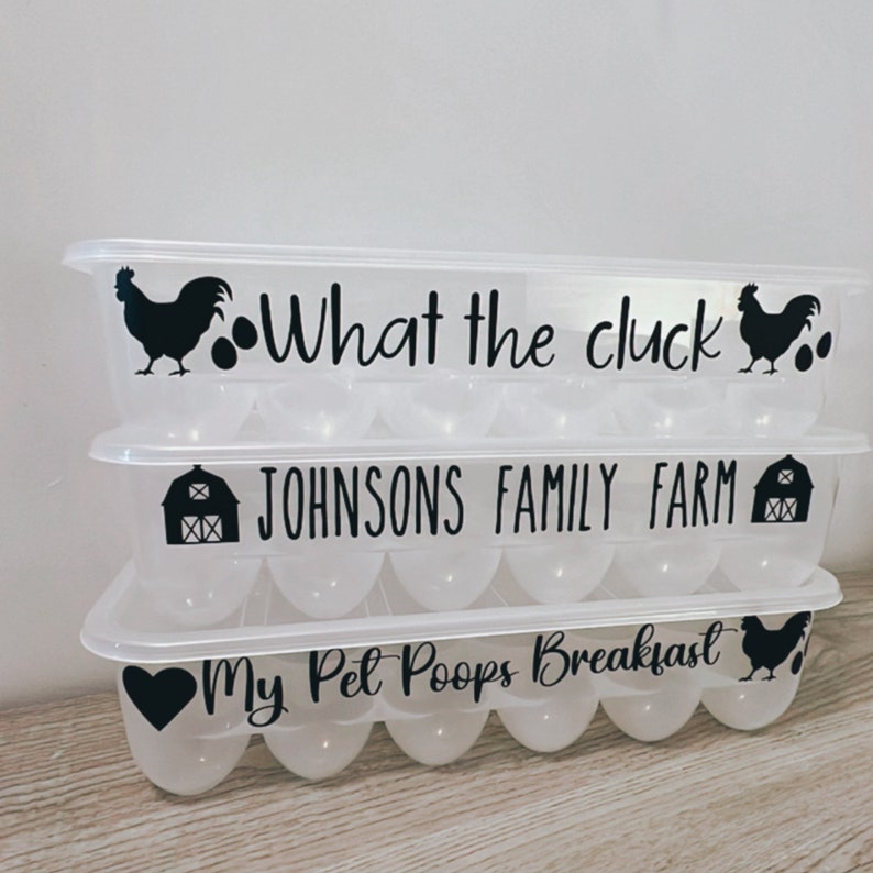 May include: Three clear plastic egg containers stacked on top of each other. Each container has a lid and is decorated with black graphics and text. The top container reads "What the cluck". The middle container reads "JOHNSONS FAMILY FARM". The bottom container reads "My Pet Poops Breakfast".