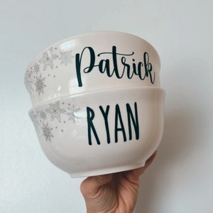 K&ouml;nnte beinhalten: Zwei wei&szlig;e Keramikschalen mit Schneeflockenmustern. Die obere Schale tr&auml;gt den Namen "Patrick" in schwarzer Schrift. Die untere Schale tr&auml;gt den Namen "Ryan" in schwarzer Schrift.
