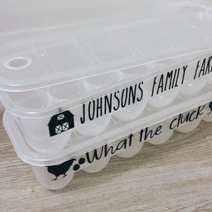 May include: Clear plastic egg container with a lid. The container has the text "JOHNSONS FAMILY FARM" and "What the cluck" in black. A black barn and chicken graphic are also visible.