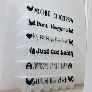 May include: A stack of clear plastic egg cartons with black text and graphics. The text includes phrases like "Mother Cluckers" and "Just Got Laid." Each carton has a different phrase and a chicken graphic.
