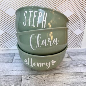 K&ouml;nnte beinhalten: Drei gr&uuml;ne Keramikschalen, die &uuml;bereinander gestapelt sind. Die Schalen sind mit den Namen "Steph", "Clara" und "Henry" in wei&szlig;er Schrift personalisiert.