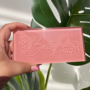 May include: A pink plastic box with a clear lid. The box features a butterfly design and the text "Boss Lashes" embossed on the front.