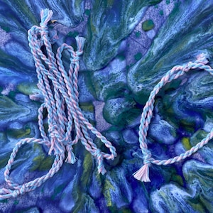 May include: Two pieces of pink and blue braided rope with knots at the ends. The rope is on a blue, green, and white marbled background.